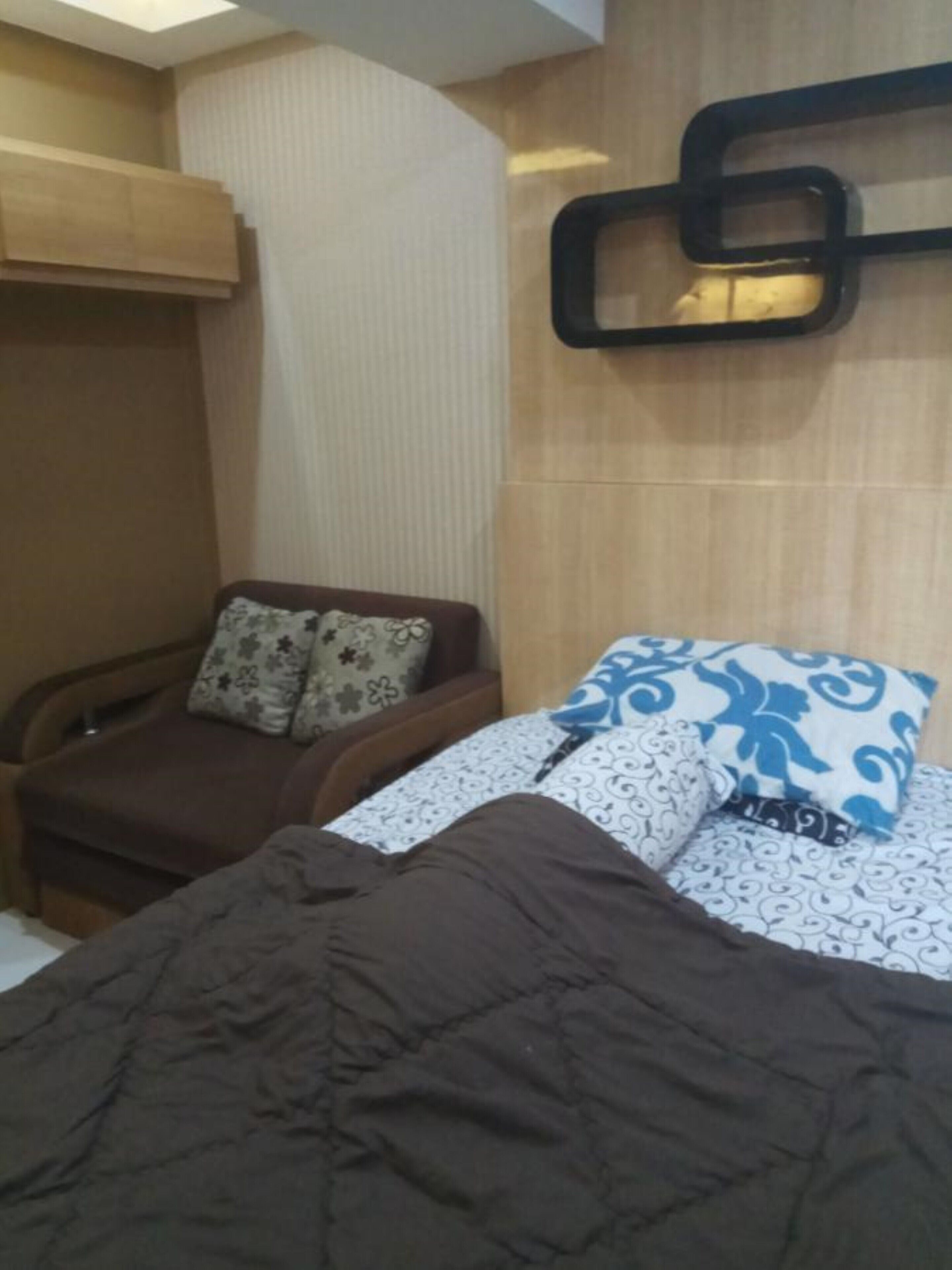 A bedroom with a bed, a sofa, and a wall-mounted shelf.
