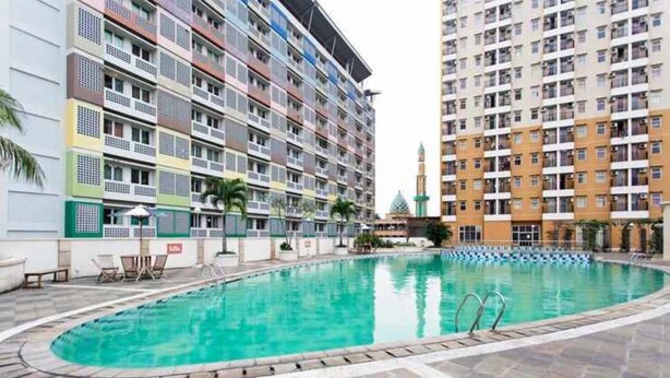Una piscina rodeada de edificios residenciales de varios pisos con balcones y una mezquita al fondo.