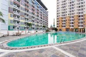 A swimming pool surrounded by multi-story residential buildings with balconies and a mosque in the background. - Sartika Apartment (Depok)