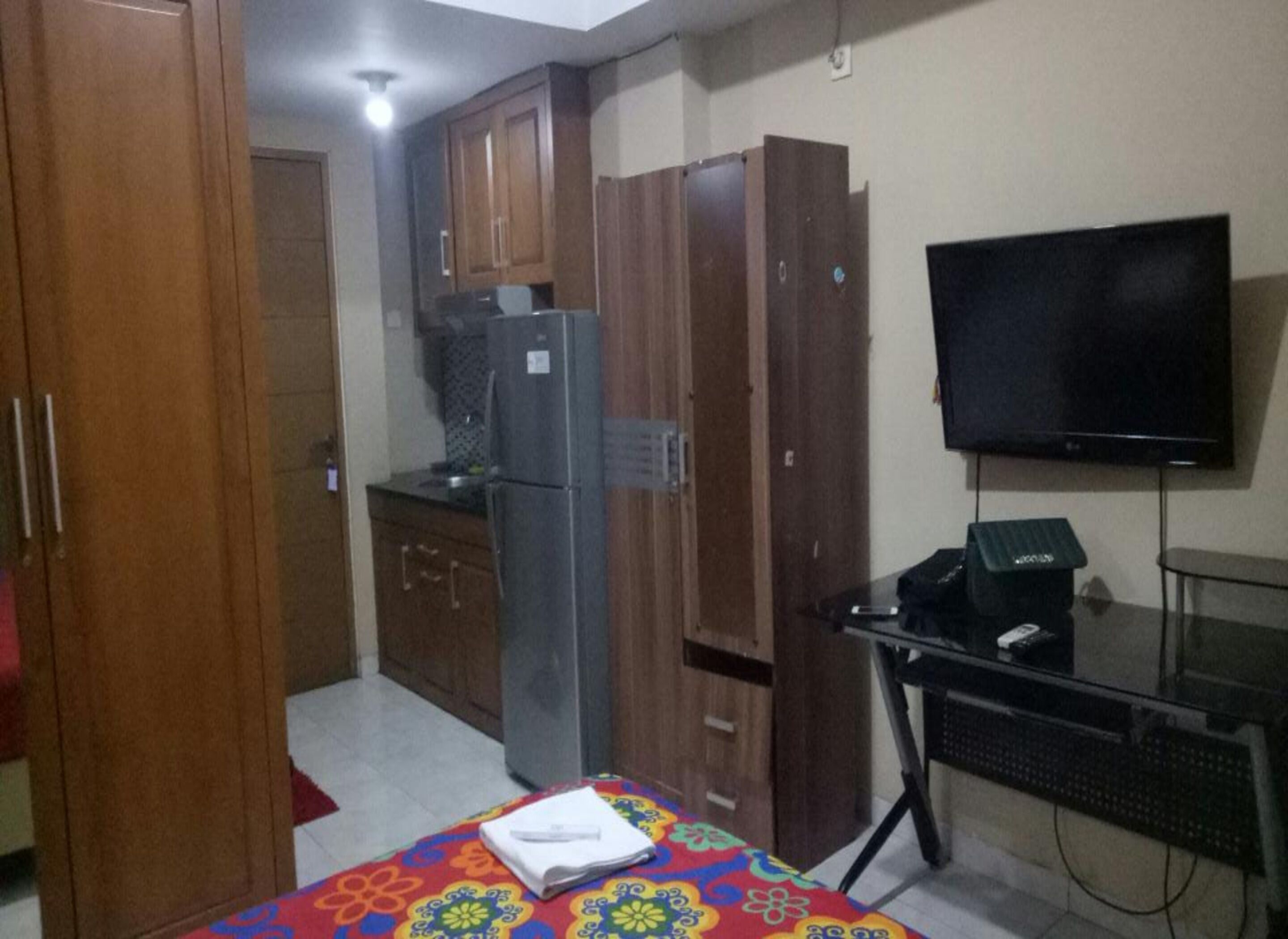 Una habitación compacta con cama, kitchenette pequeña, televisor y escritorio.