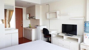 Habitación de hotel compacta con cama, escritorio, computadora, televisión, kitchenette y baño.