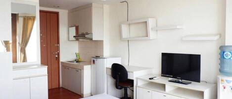 A compact hotel room with a bed, a desk with a computer and TV, a small kitchenette, and a bathroom.