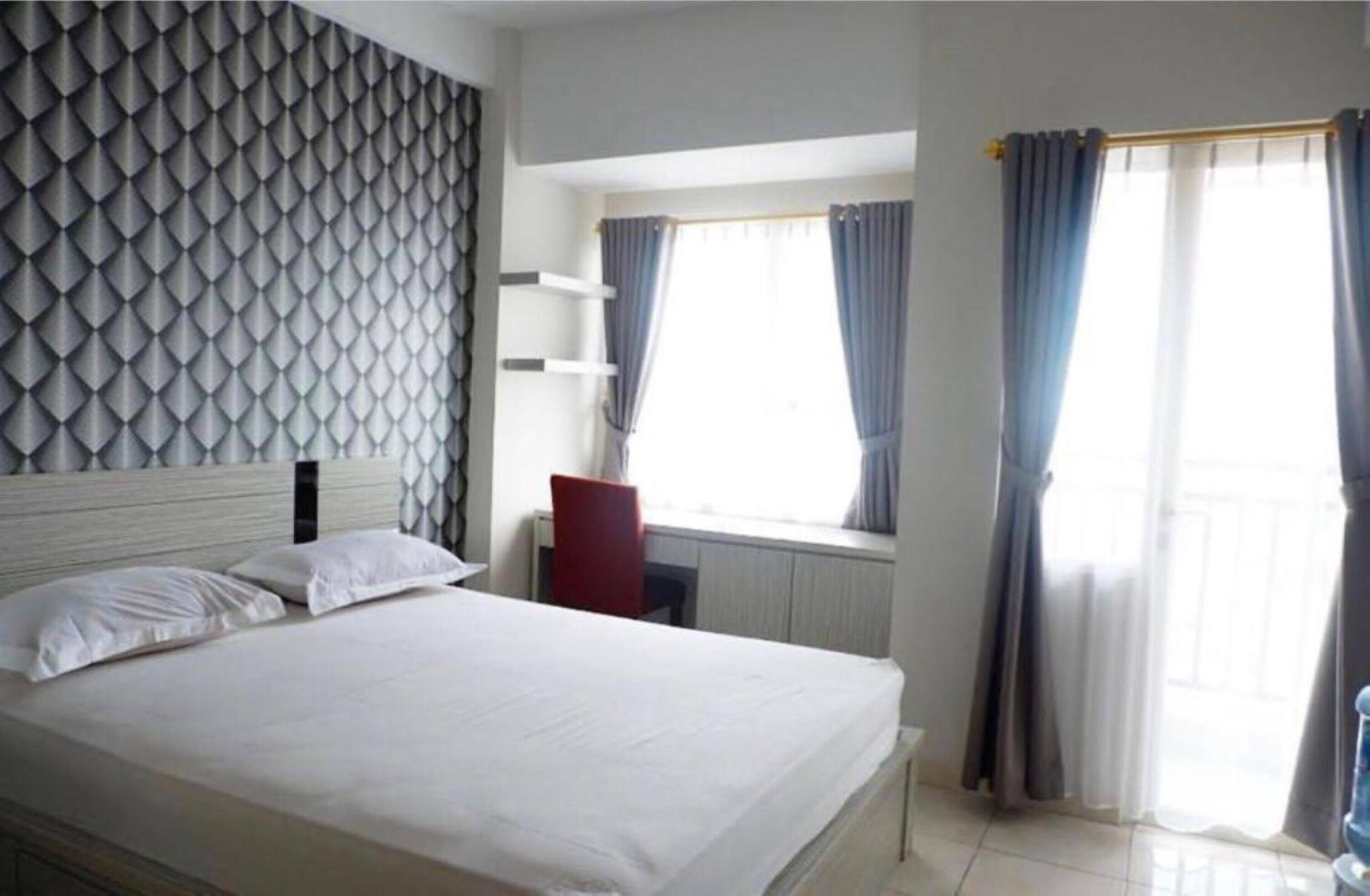 A neatly made bed with white linens, a headboard with a geometric pattern, and a window with curtains.