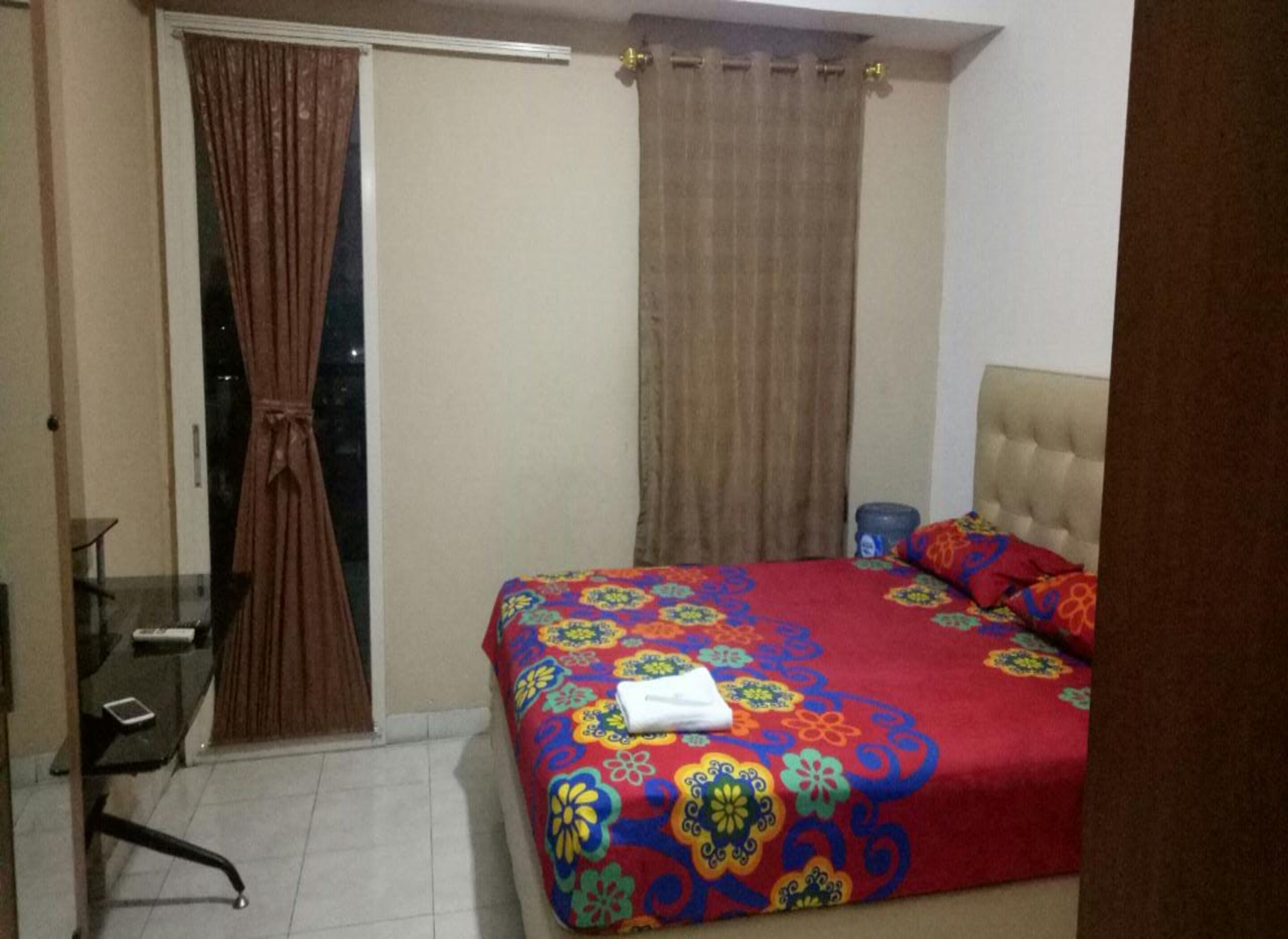 Quarto com cama, cadeira, mesa e janela com cortinas.
