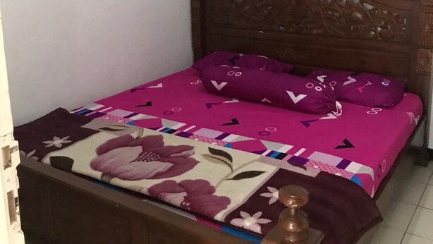 A single bed with a wooden headboard, a floral-patterned bedspread, and matching pillows. - Villa 3 Putri 27 (Batu)
