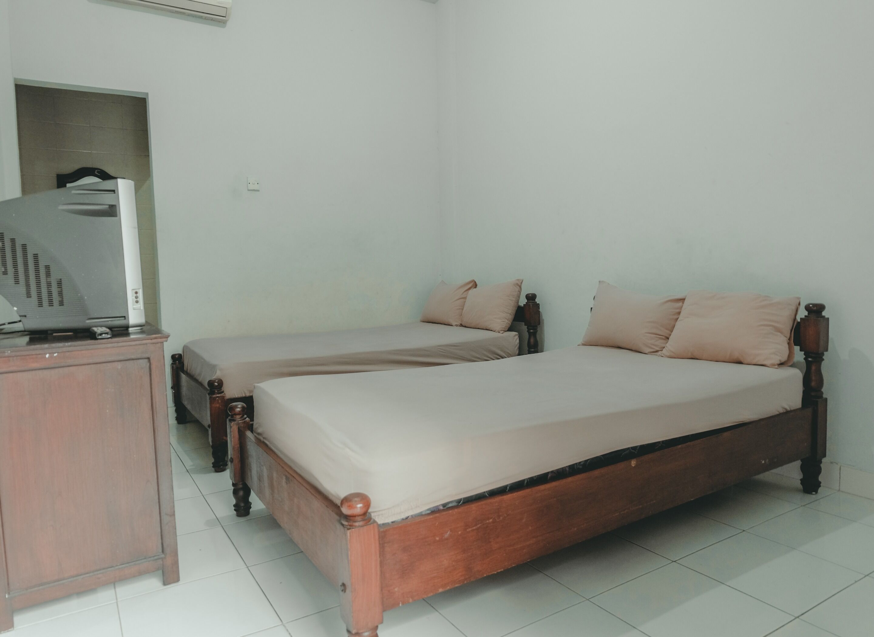 A bedroom with two single beds, a wooden dresser, and a television on a stand.