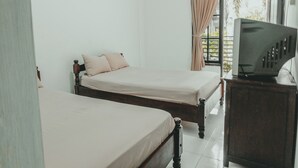 Un dormitorio con dos camas individuales, un televisor sobre un mueble de madera y una ventana con cortinas.