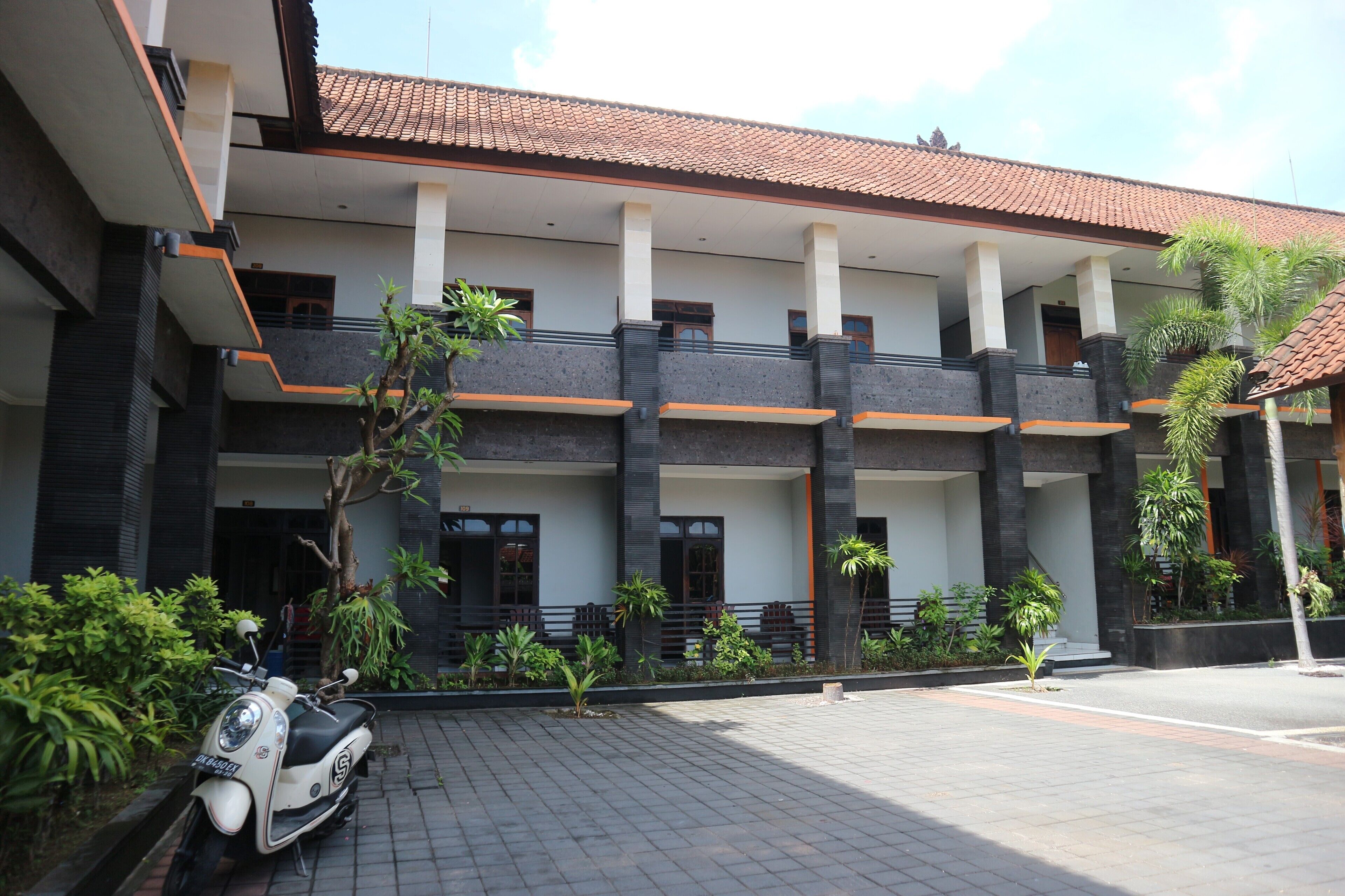 Un edificio moderno con tetto in tegole, diversi balconi e un'area d'ingresso pavimentata con uno scooter parcheggiato.