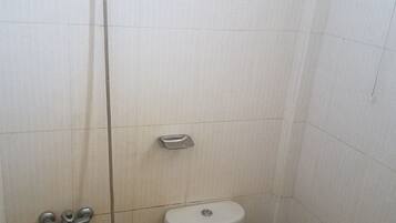 A small, compact bathroom with a toilet, a shower head, and a hand basin.