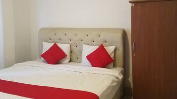 A neatly made bed with a red and white bedspread, a wooden wardrobe, and a small brown ottoman.