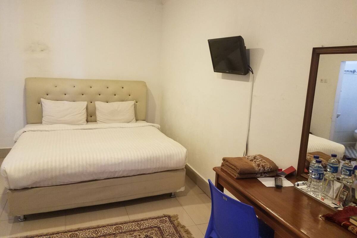 A bedroom with a bed, a desk with a mirror, and a TV mounted on the wall.