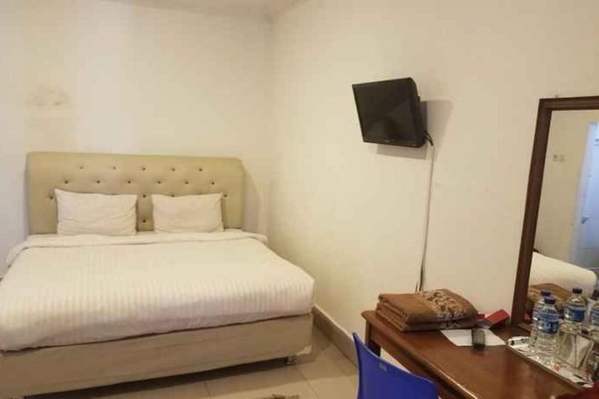 A bedroom with a bed, a desk, a chair, a television, and a mirror.
