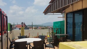 Une terrasse sur le toit, avec une table ronde et des chaises, un fond vert et une vue sur la ville et les montagnes.
