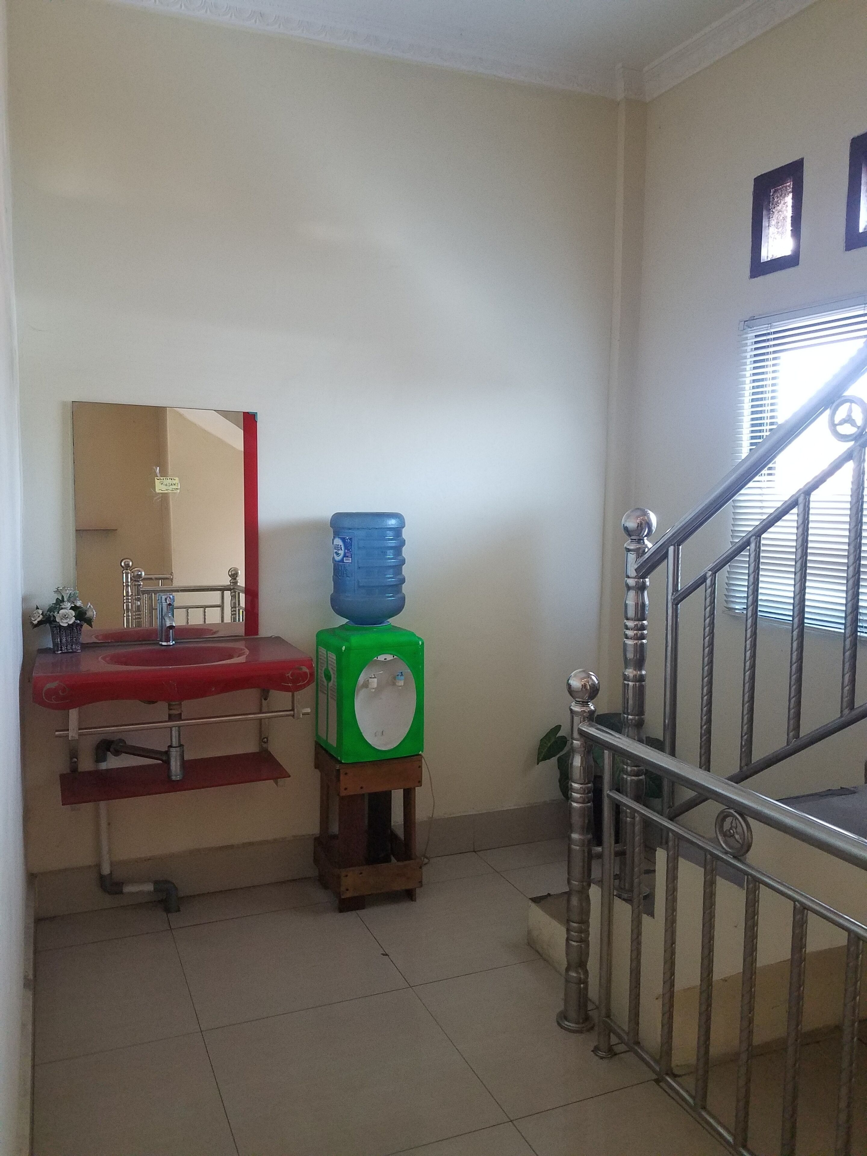 A bathroom with a red sink, a mirror, a green water dispenser, and a staircase with a metal railing.