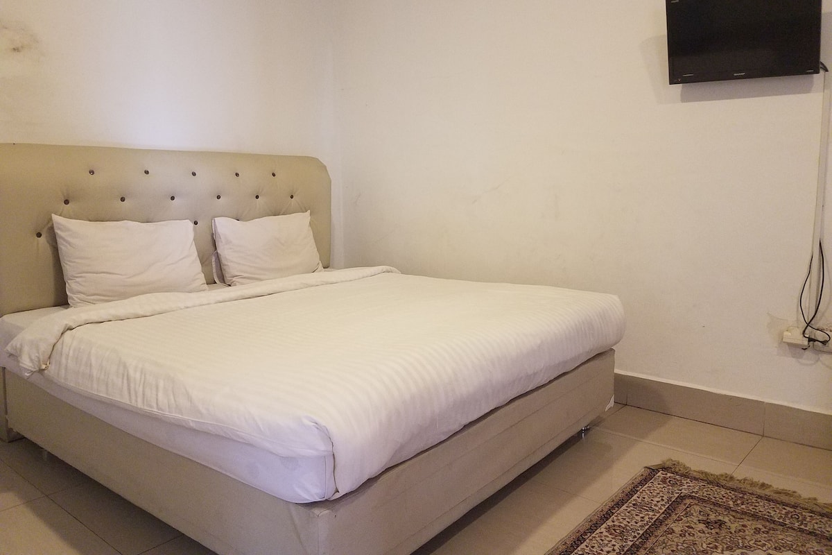 A bed with a headboard, two pillows, and a flat-screen TV mounted on the wall.