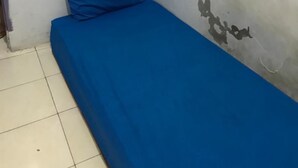A small room with a single bed, a white wall with peeling paint, and a tiled floor. - Kost Aka (Makassar)