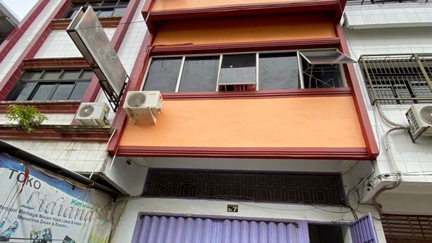 A multi-story building with a red and white facade, a purple entrance gate, and a parked car in front. - Kost Aka (Makassar)