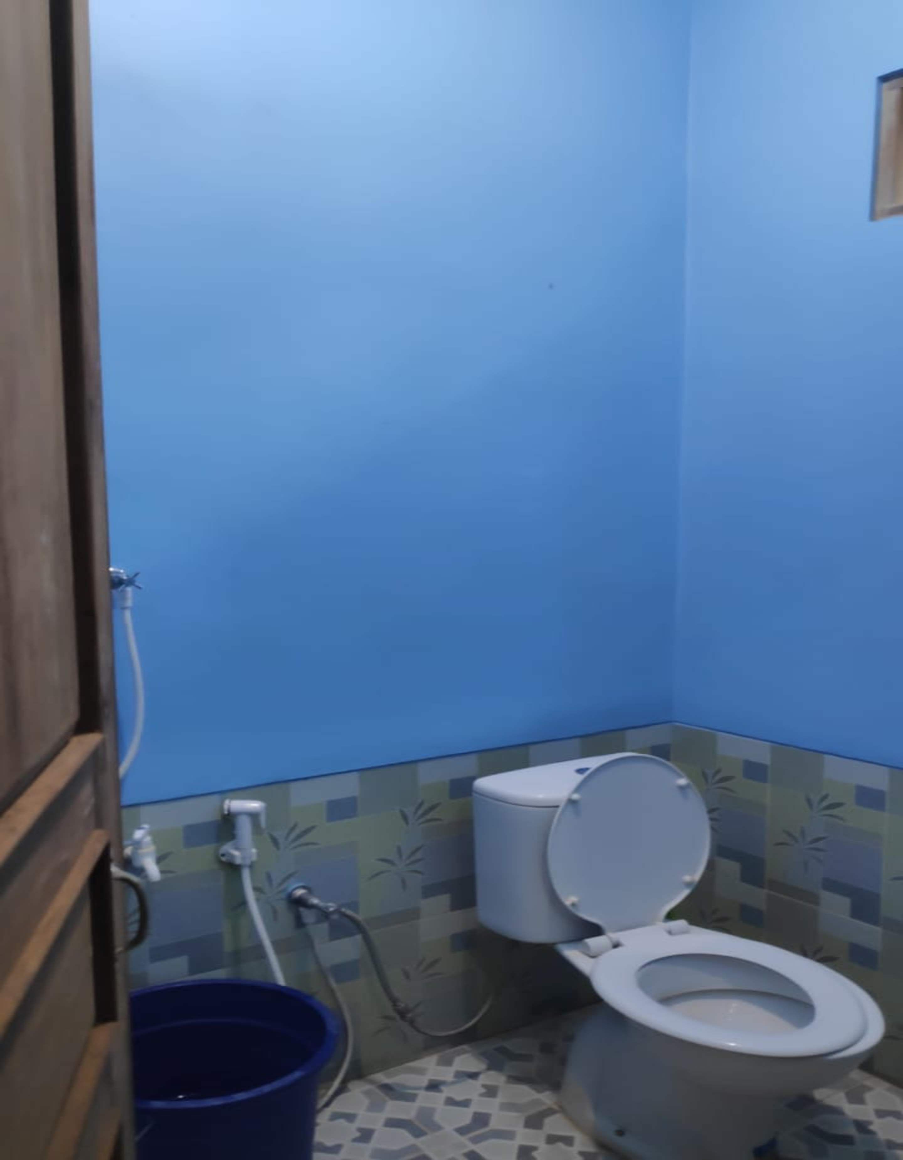A small bathroom with a toilet, a blue bucket, and a shower head.