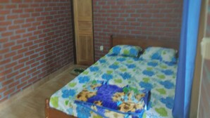 Una habitación pequeña con pared de ladrillo, puerta de madera y cama con colcha estampada de flores.