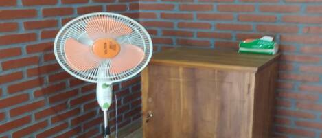 Una habitación de esquina con pared de ladrillo, un armario de madera y un ventilador de pie.