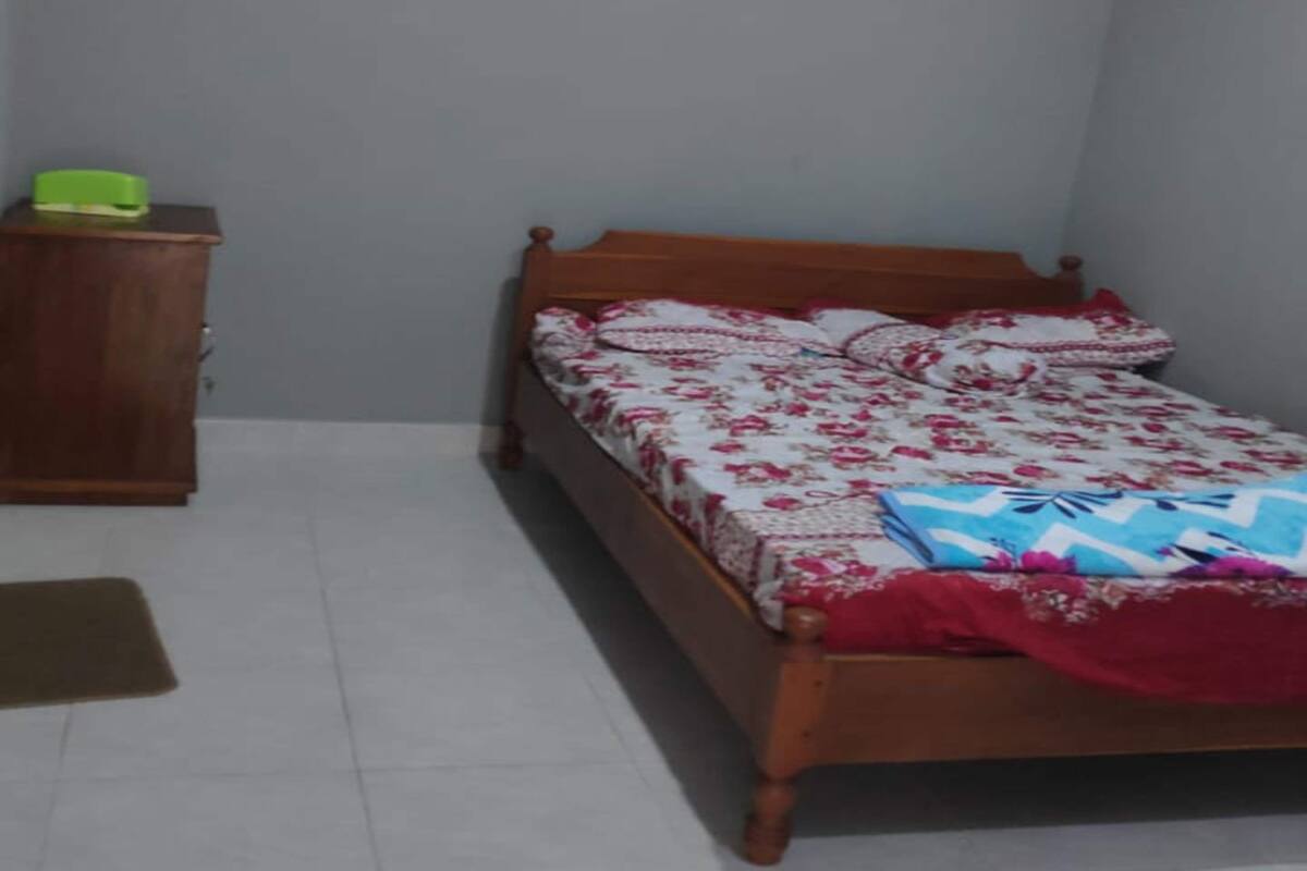A bedroom with a bed, a nightstand, a small window, and a green object on the nightstand.