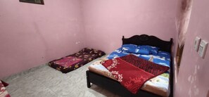 A small, pink-walled room with a single bed featuring a blue and red bedspread, a wooden headboard, and a small bedside table. - Wahyu Utomo Syariah (Tawangmangu)
