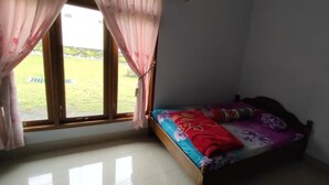 A small room with a bed, a window with curtains, and a view of a grassy area outside. - Wahyu Utomo Syariah (Tawangmangu)