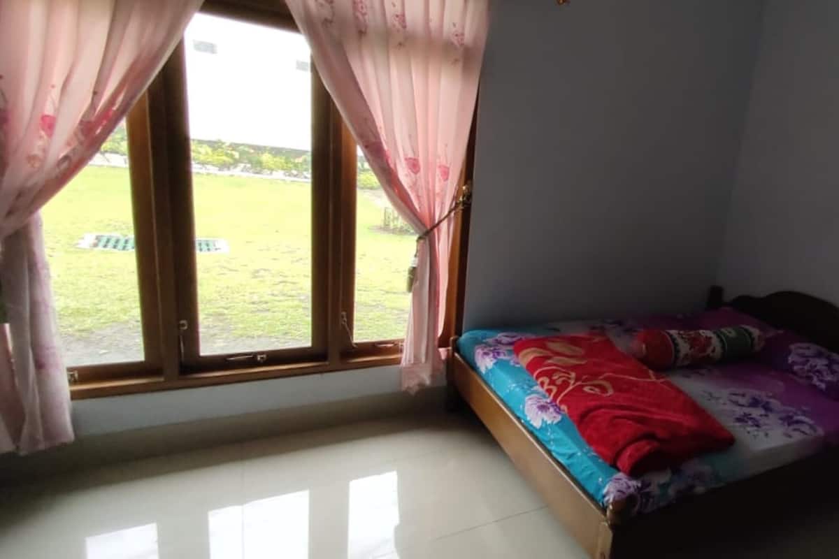 A small room with a bed, a window with curtains, and a view of a grassy area outside.
