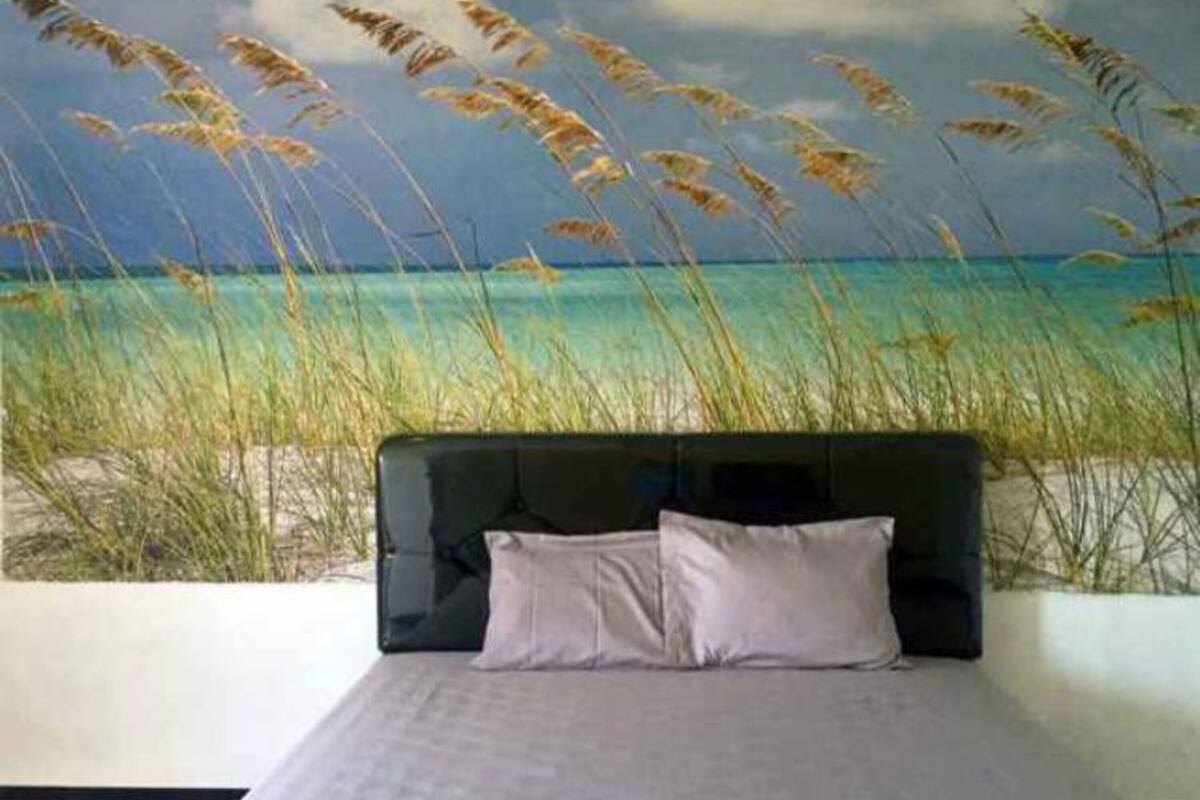 A bedroom with a bed, pillows, and a wall mural of a beach scene.