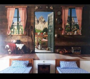 A room with two beds, a wooden door leading to a scenic outdoor view, and a rustic interior with checkered curtains and wall-mounted clocks. - D'Sawah Homestay (Klaten)