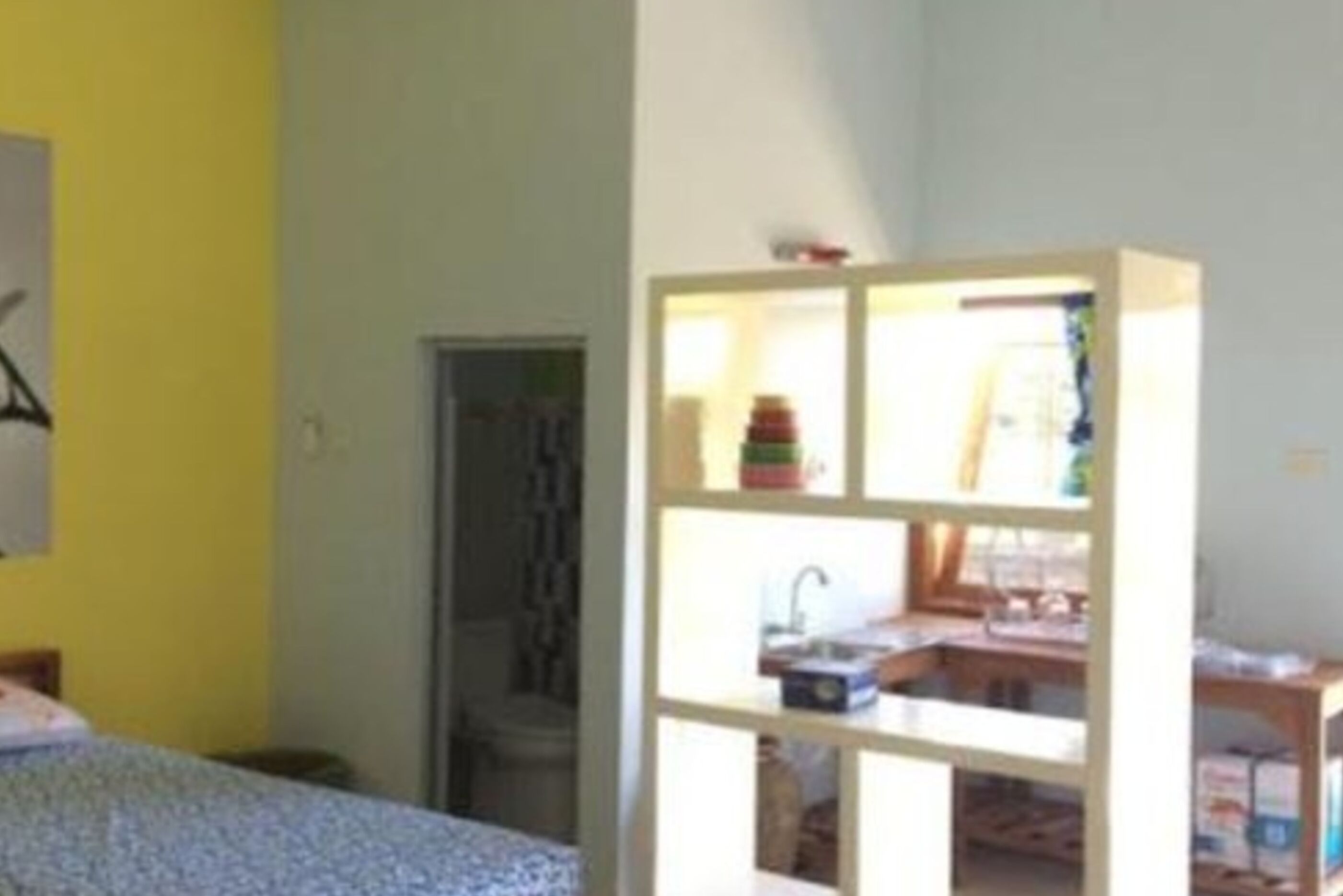 Una habitación con una cama, una estantería blanca con compartimentos y una ventana.