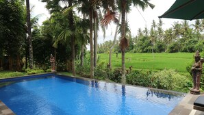 A swimming pool with a view of a lush garden and palm trees. - Pondok Tulasi Semaya House (Sukawati)