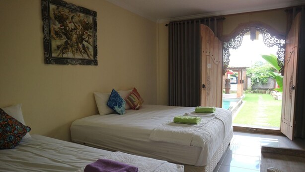 A hotel room with two beds, a painting on the wall, and a view of the outside. - Pondok Tulasi Semaya House (Sukawati)