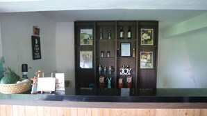 A bar area with a wooden counter, shelves with bottles, and a 'JOY' sign. - Pondok Tulasi Semaya House (Sukawati)