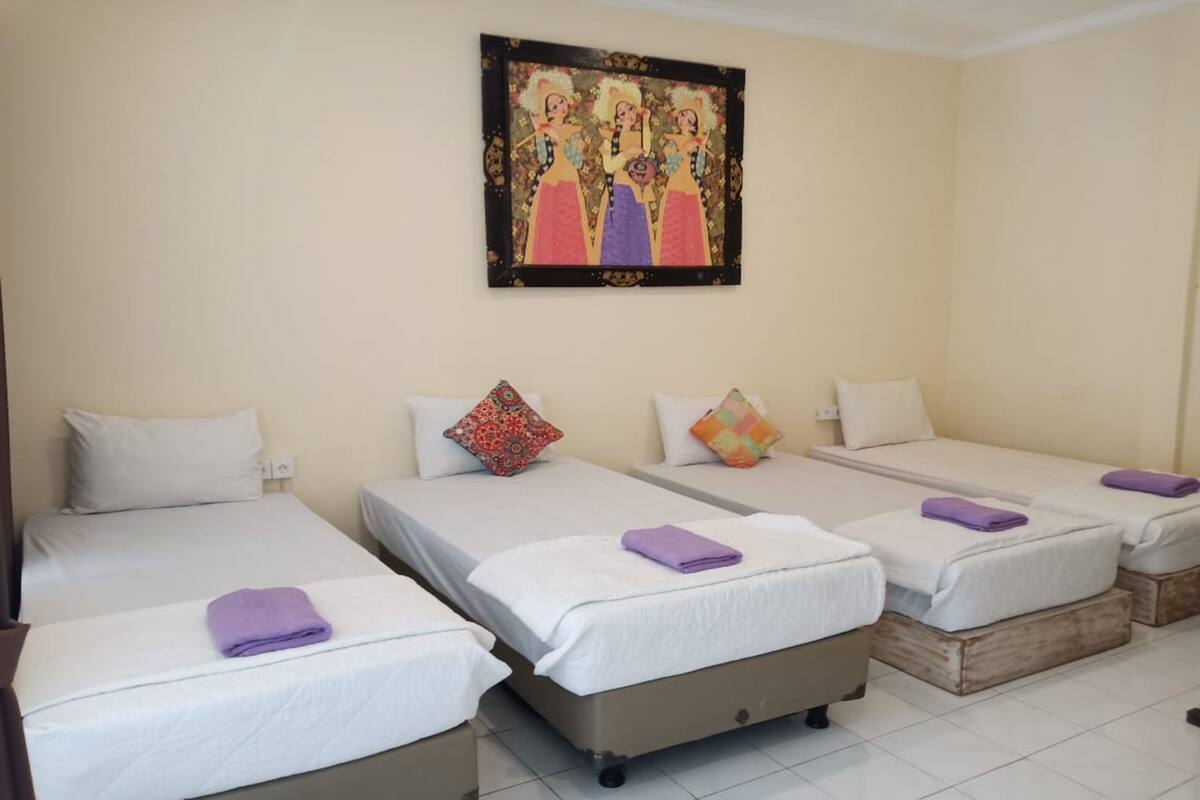 Hotelkamer met drie eenpersoonsbedden, elk met een witte matras en een paarse handdoek. Daarboven hangt een ingelijst kunstwerk en de kamer heeft een neutraal kleurenpalet.