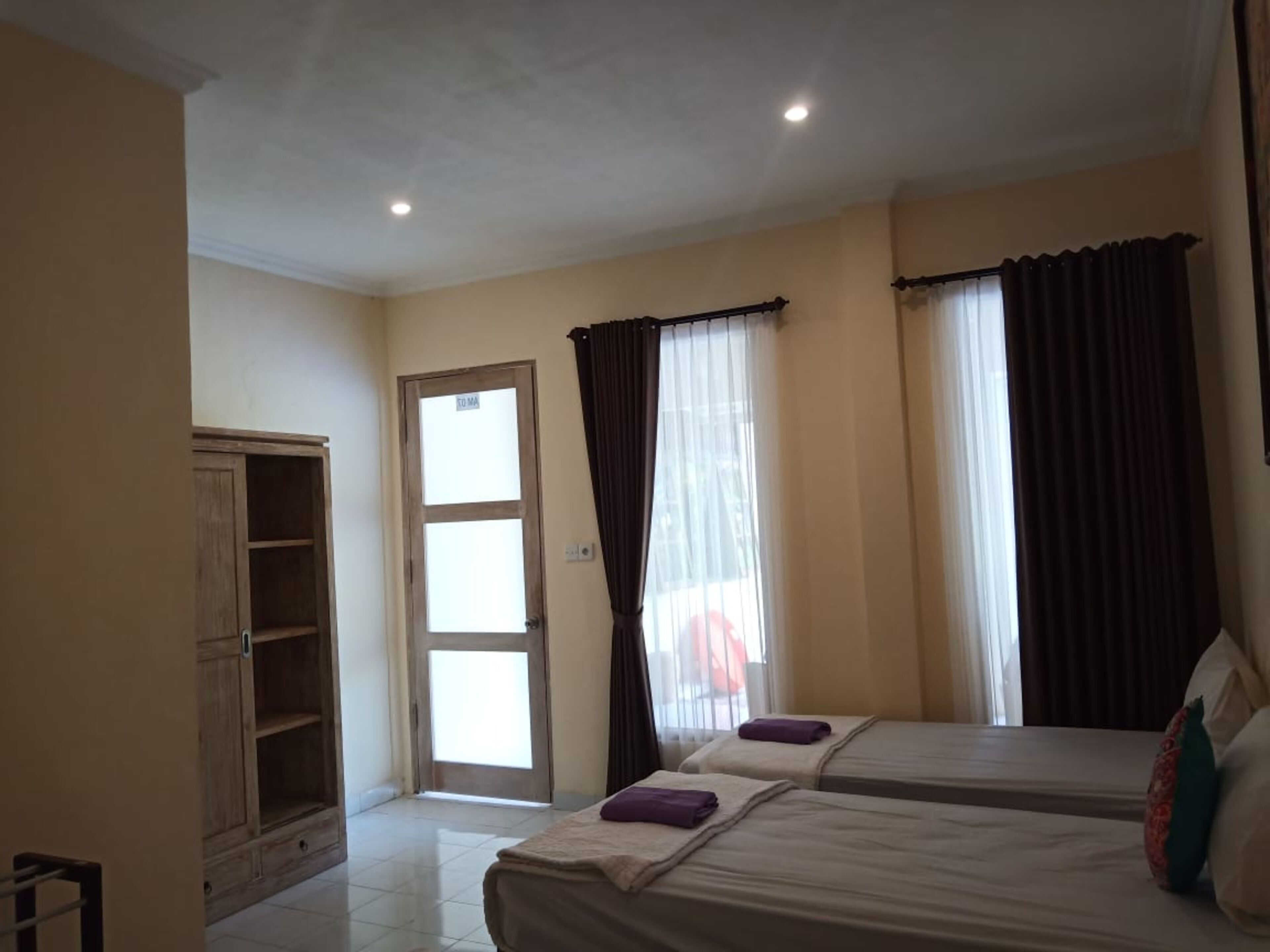 A room with two beds, a wooden wardrobe, a door, and a window with curtains.