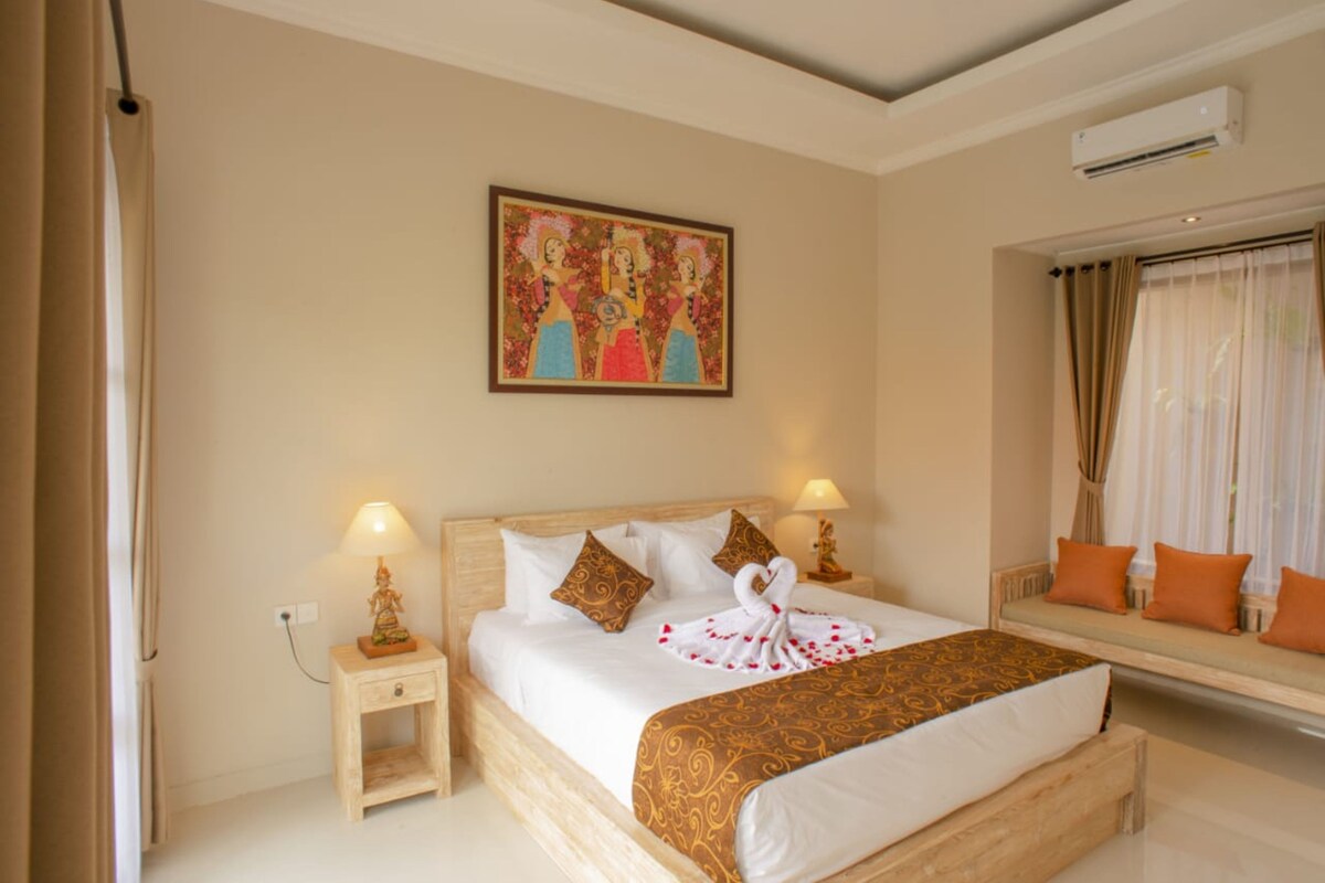 Camera d'albergo con un letto, abat-jour, comodino, un quadro appeso e una finestra con tende.