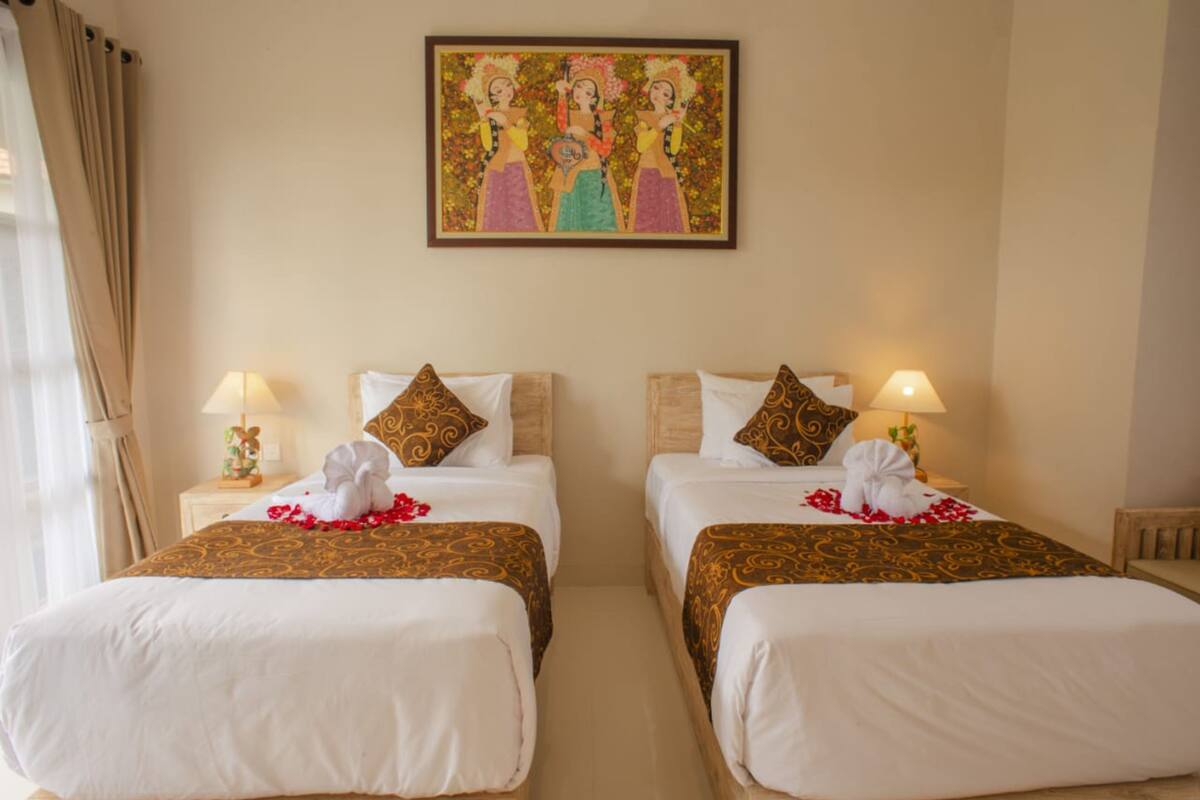 Een hotelkamer met twee bedden, elk met een kussen en een lamp. Boven de bedden hangt een schilderij aan de muur.