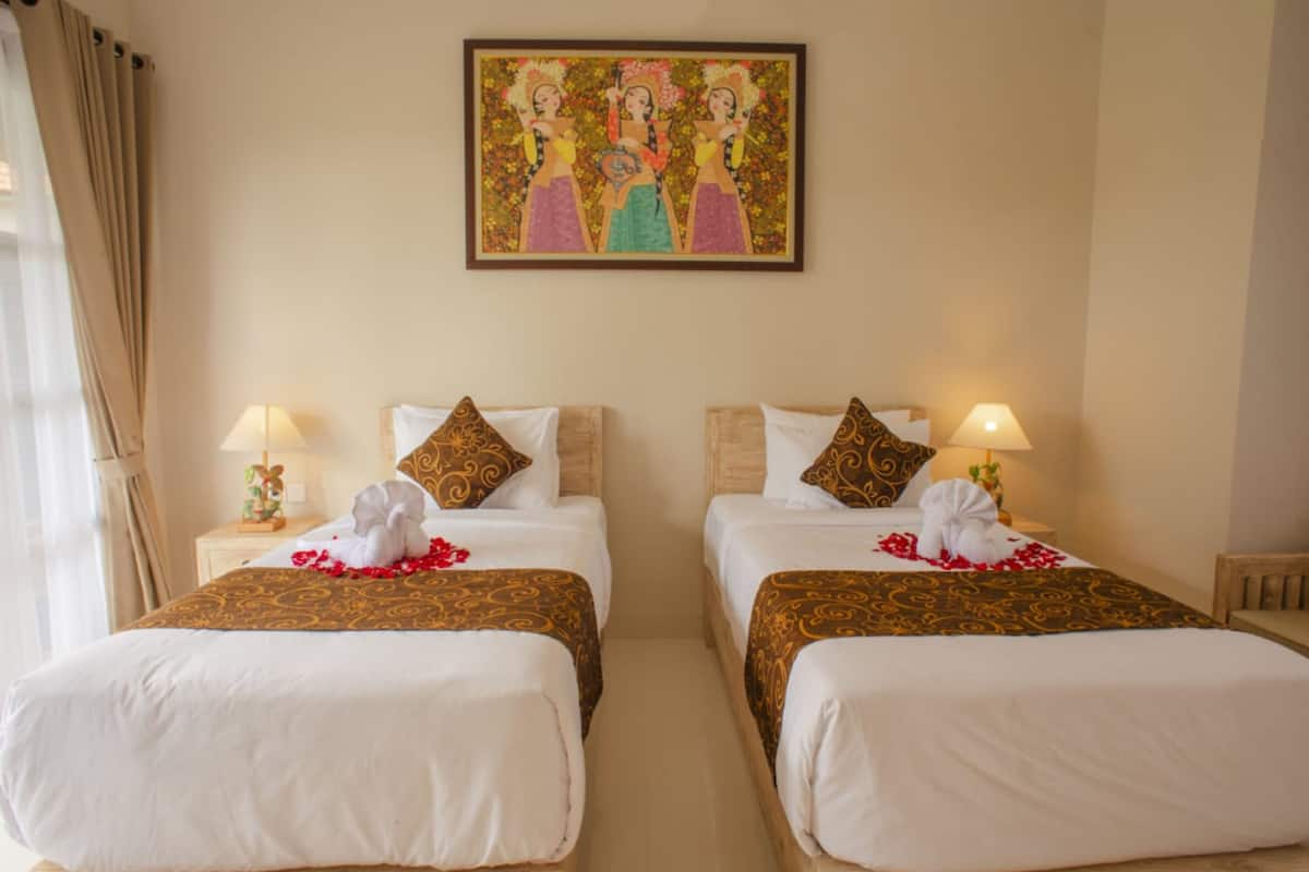 A hotel room with two beds, each with a pillow and a lamp. There is a painting on the wall above the beds.