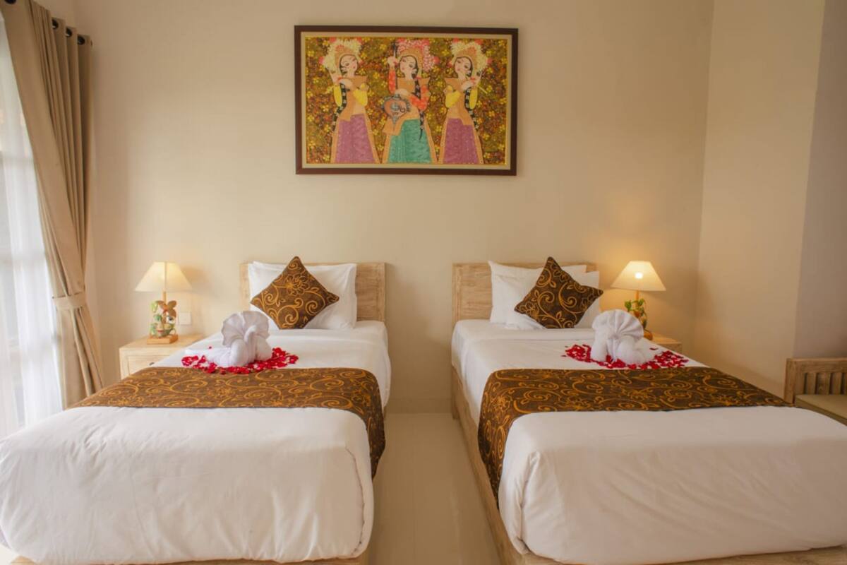 Een hotelkamer met twee bedden, elk voorzien van een witte spreidek en een decoratief kussen. Boven de bedden hangt een schilderij, en op elk nachtkastje staat een lamp.