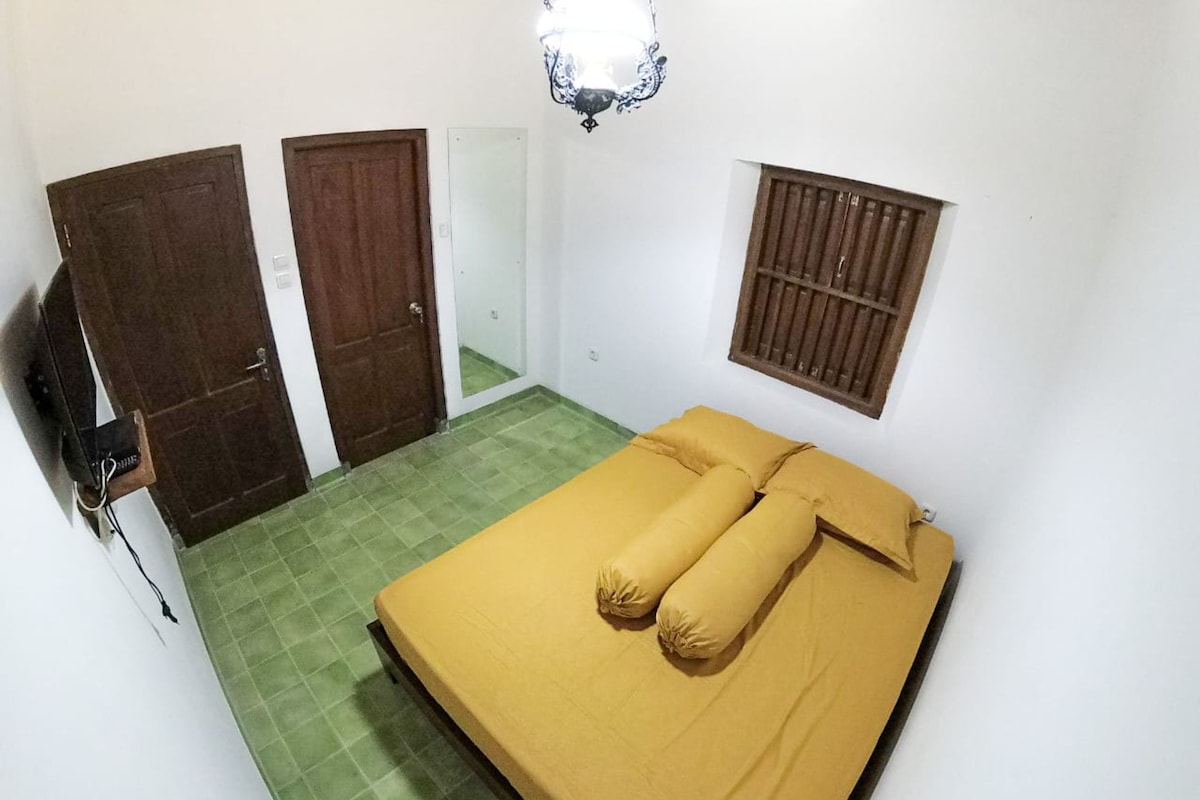 A room with a bed, two doors, a window with bars, and a light fixture.