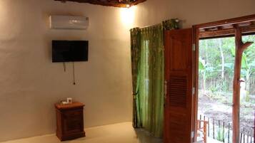 Una habitación con una cama, televisión montada en la pared, una mesita de noche de madera y una ventana con cortinas verdes.