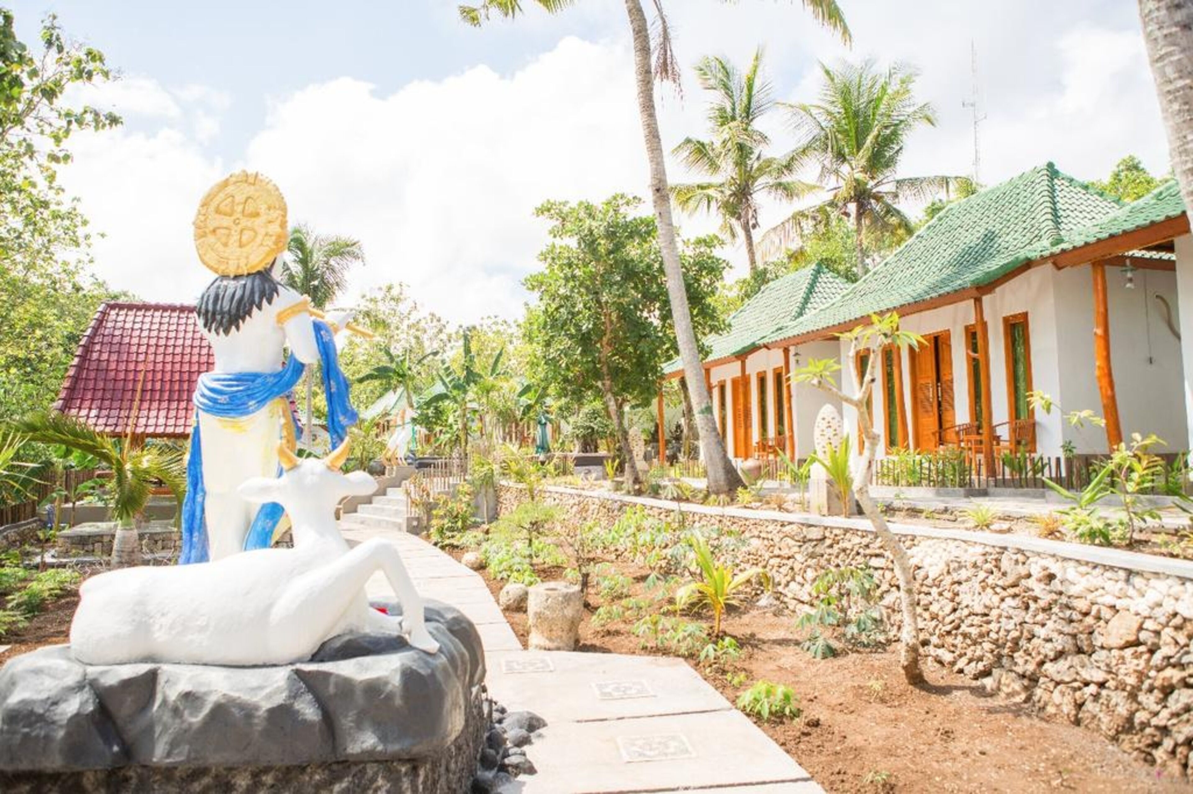 A tropical resort with a statue of a woman holding a coin, a white swan sculpture, and a traditional house with a green roof.