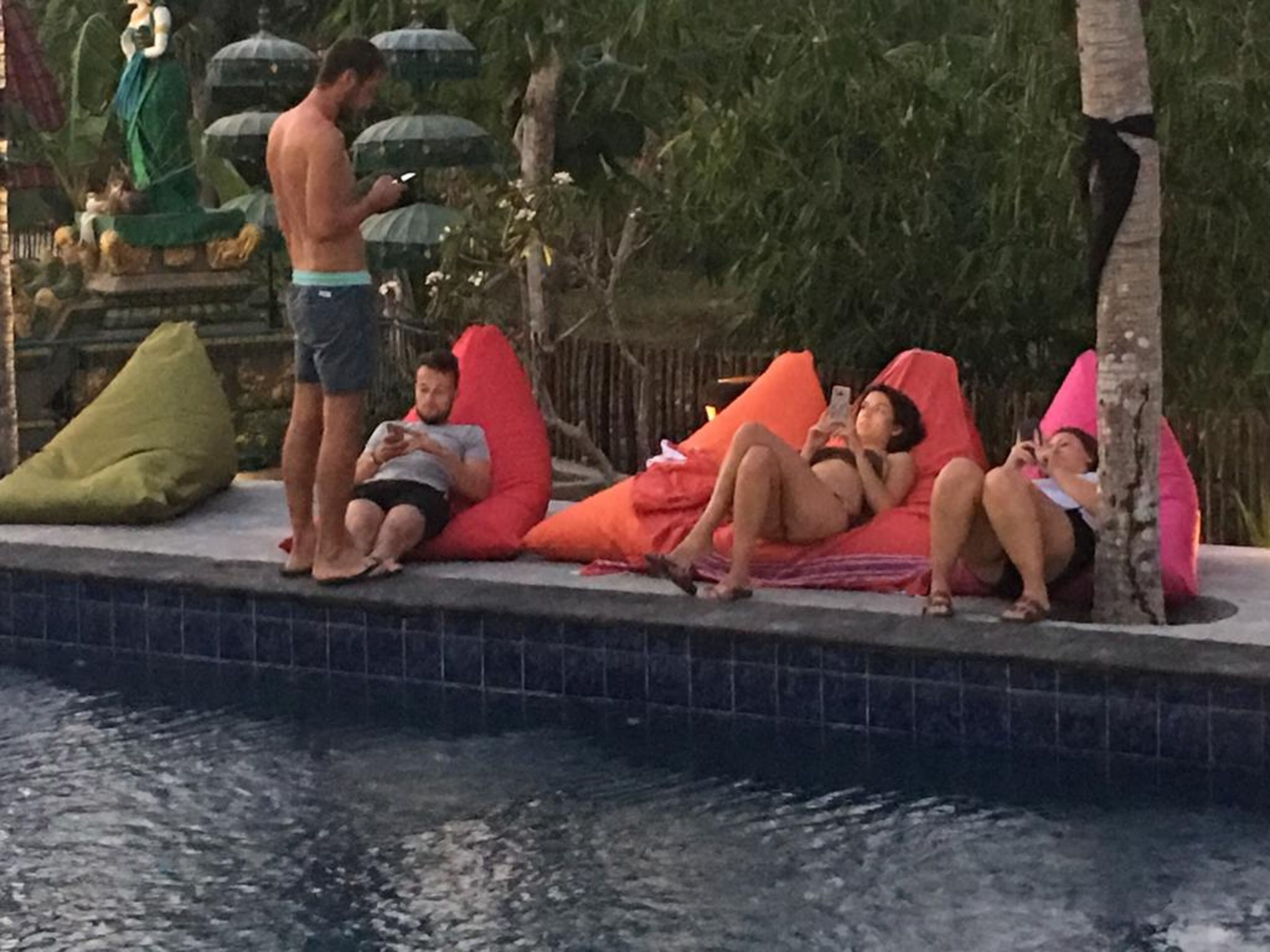 A poolside area with a tiled edge, a statue, and people relaxing on bean bags.