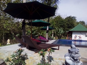 Zona de piscina con sillones de descanso, sombrillas y una estatua.