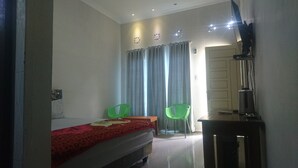 Une chambre à coucher avec un lit, deux fauteuils verts, un bureau avec un ordinateur et un radiateur.