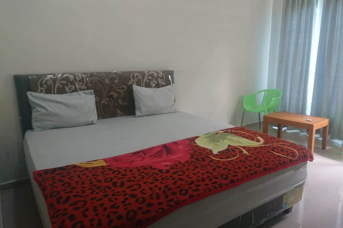 Une chambre d’hôtel avec un lit, une petite table, deux chaises vertes et une fenêtre avec des rideaux.