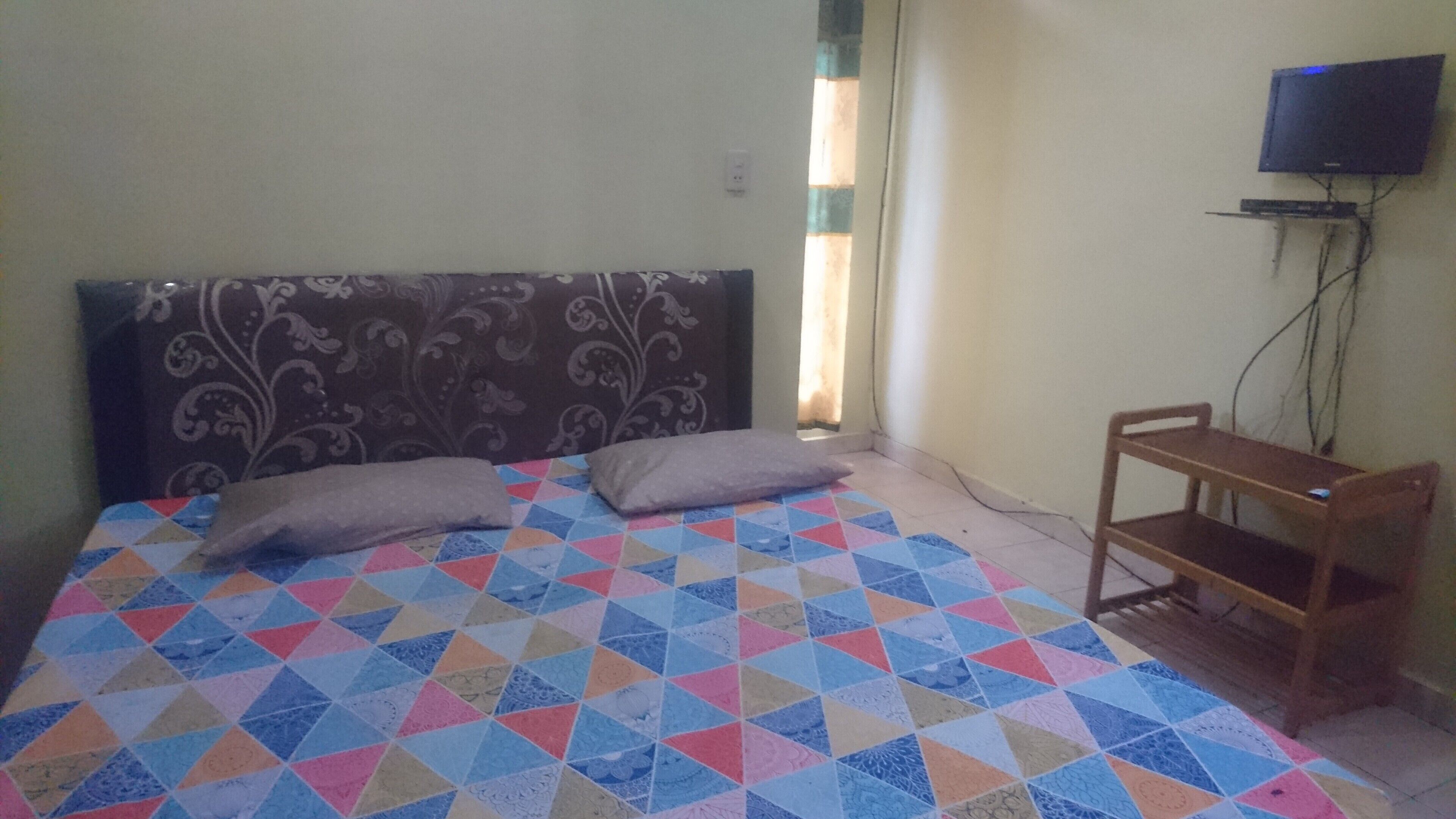 A bedroom with a bed, pillows, a TV, and a small wooden table.