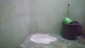 A small bathroom with a toilet, a trash bin, and a green bucket.