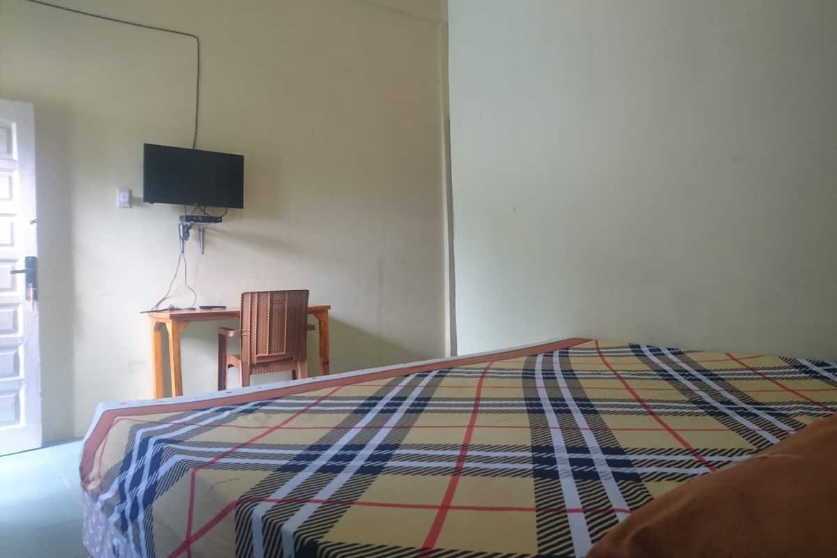 A room with a bed, a television mounted on the wall, a small wooden table, and a chair.